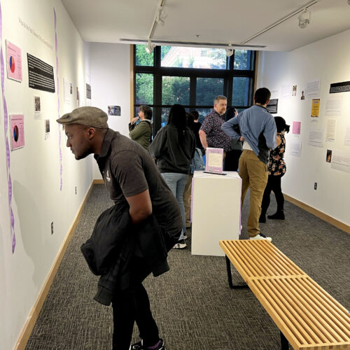 A crowd studies the exhibit “Sweeter Than the Onions: Stories of Queer Resilience in Walla Walla,” at Whitman College. (Credit: Courtney Flatt, Northwest News Network)