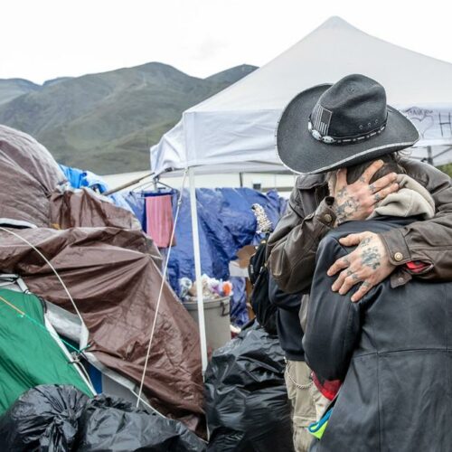 A man hugs another person in front of tents at a homeless camp in Clarkston.