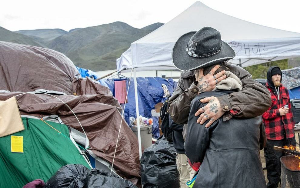 A man hugs another person in front of tents at a homeless camp in Clarkston.