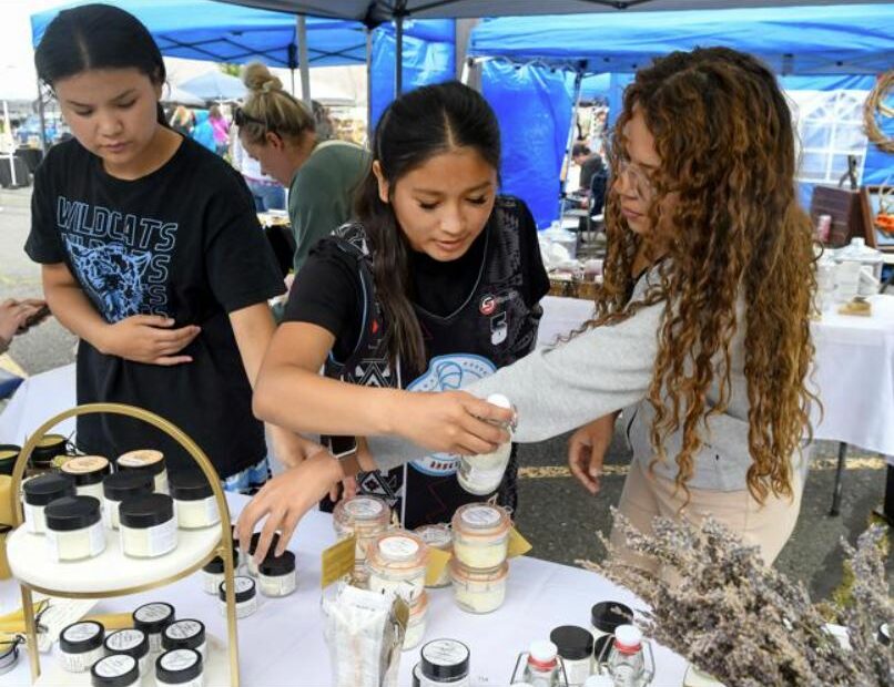 From left to right: Sisters Charlie Kipp, Michelle Kipp and Jessie Kipp cross arms as they shop goods at the Pure Glam vendor tent at the Lewiston Farmers Market on Saturday, June 15. (Credit: Liesbeth Powers/Moscow-Pullman Daily News)