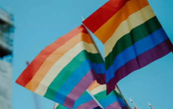 Pride flags fly in the wind against a clear blue sky