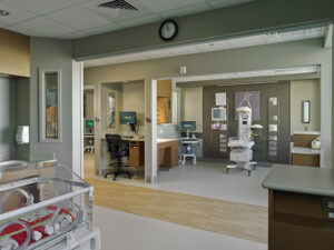 A small incubator for premature babies is in the right hand corner of the photo. A wooden hallway is in the center of the photo. On the other side of the hallway is another incubator.