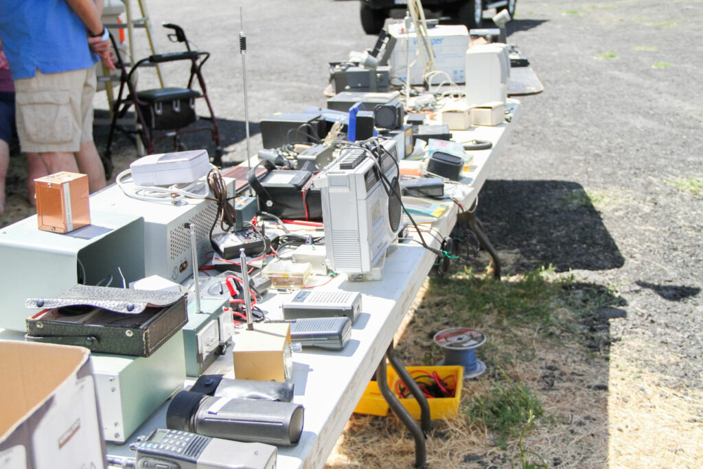 A large quantity of radio equipment is set out on a folding table outside.