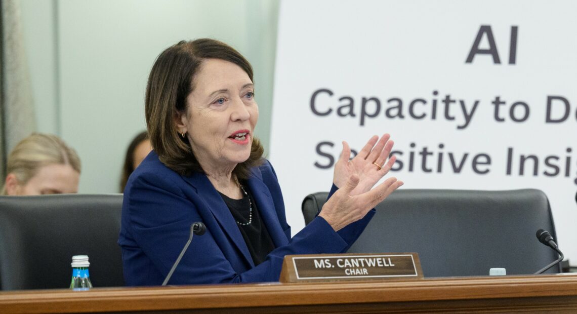 U.S. Senator Maria Cantwell talks into a microphone at a brown wooden podium about AI while wearing a dark blue blazer.