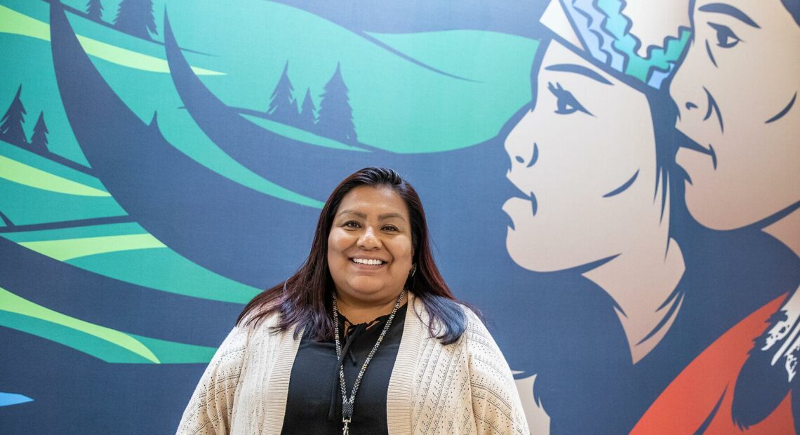 Roberta José-Bisbee stands for a portrait in front of a mural.