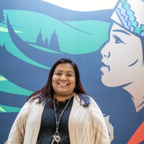 Roberta José-Bisbee stands for a portrait in front of a mural.