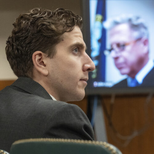 A photo shows the side profile of Bryan Kohberger, who has pale skin and dark hair. A video screen with the gray-haird Judge John Judge on display is in the background.