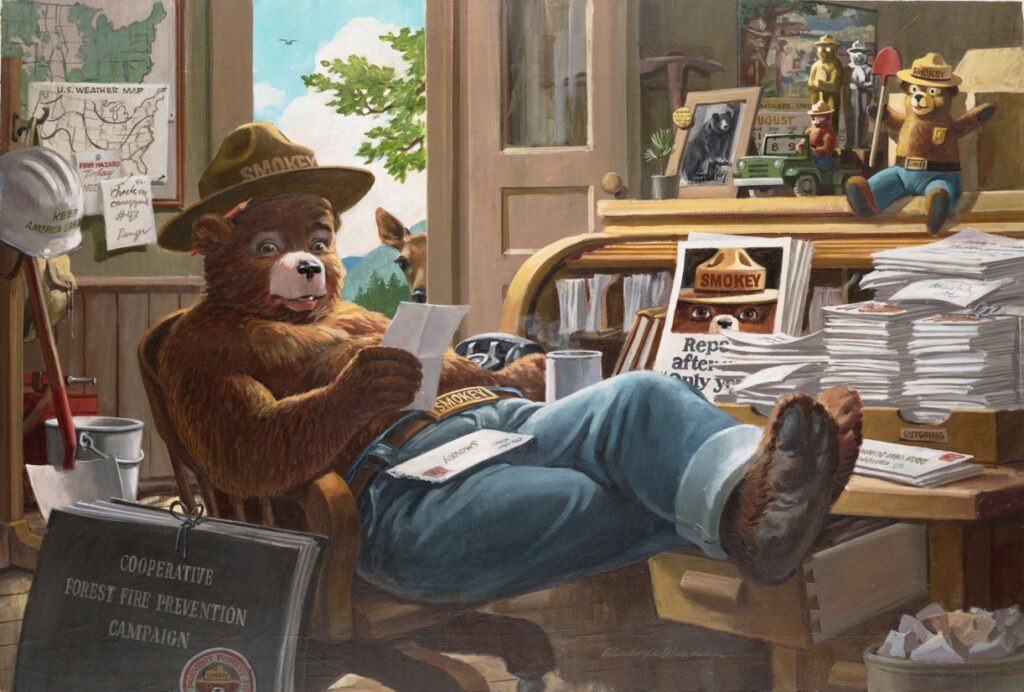 Smokey Bear reclines in a chair at a wooden desk covered in white envelopes. He reads a fan letter in his chair. 