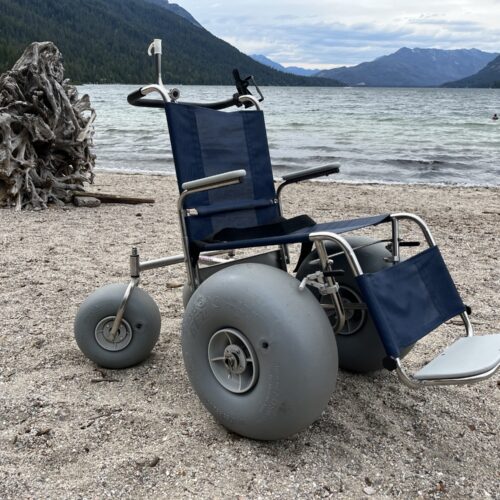 A blue beach wheelchair, with three large gray tires, sits on a beach at Lake Wenatchee.