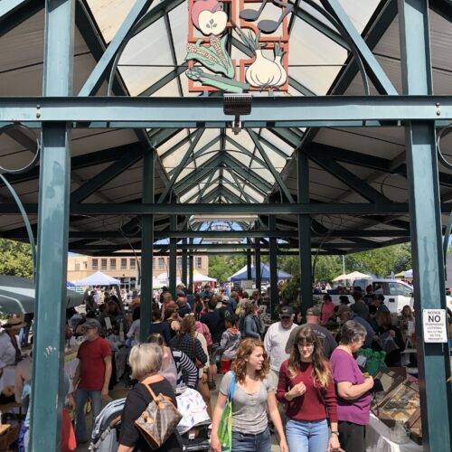 A group of people walk through vendor stalls at the Walla Walla Downtown Farmers market.