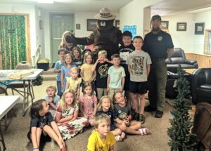 Smokey Bear stands behind a group of children smiling for the camera at the Weippe Library.