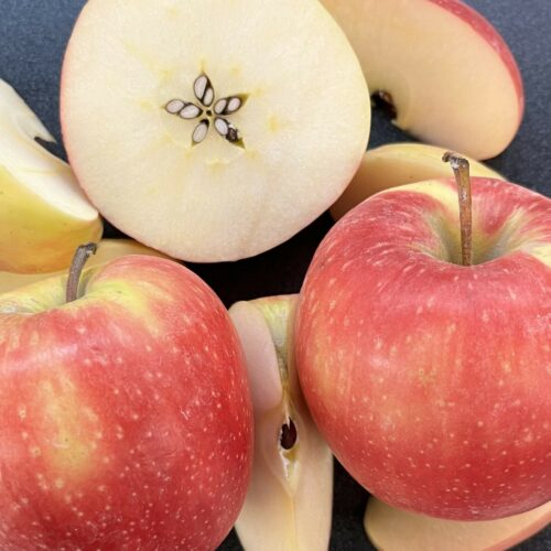 The photo shows whole apples covered in light orange, yellow and blush skin. Some apples are sliced open to reveal a white interior.