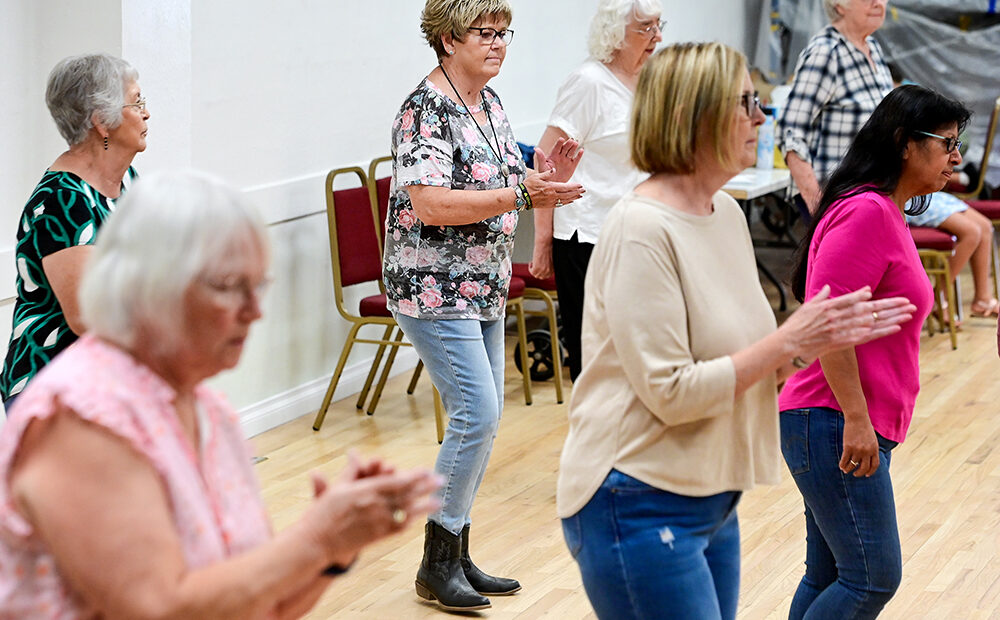 Seven people, divided into two lines, practice a line dance routine.