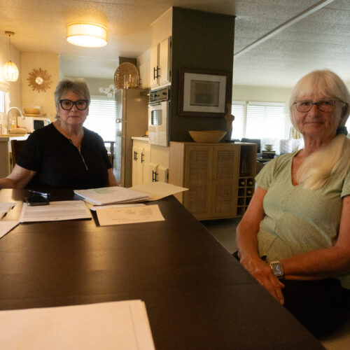 Two women look at the camera with papers before them.