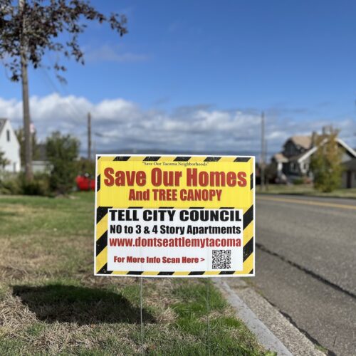 A bright yellow and black sign is placed in a front yard. Some of the text, in red letters, reads: "Save our homes and tree canopy."