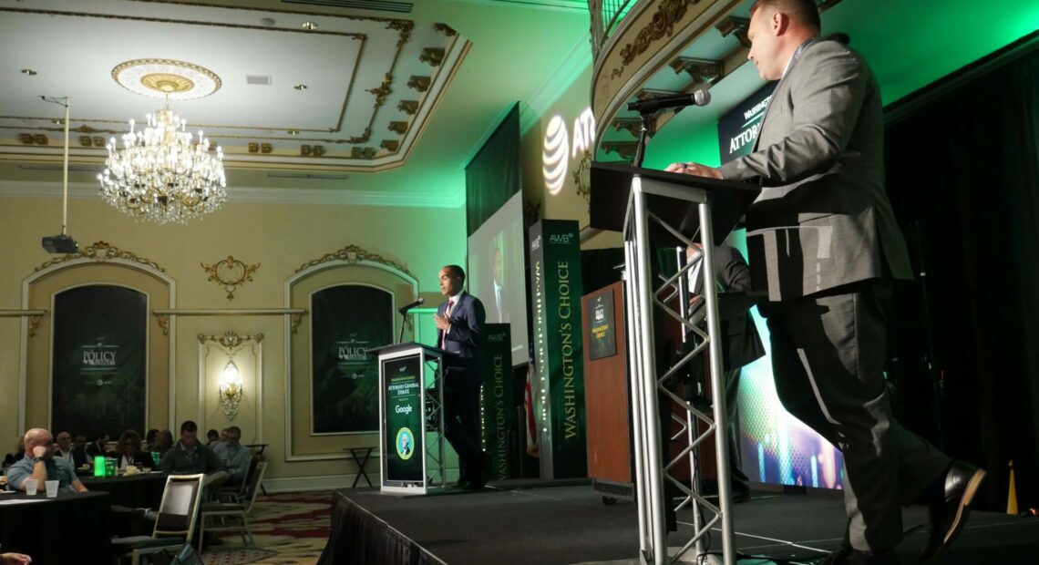 Two men, each behind a podium, stand on a stage.