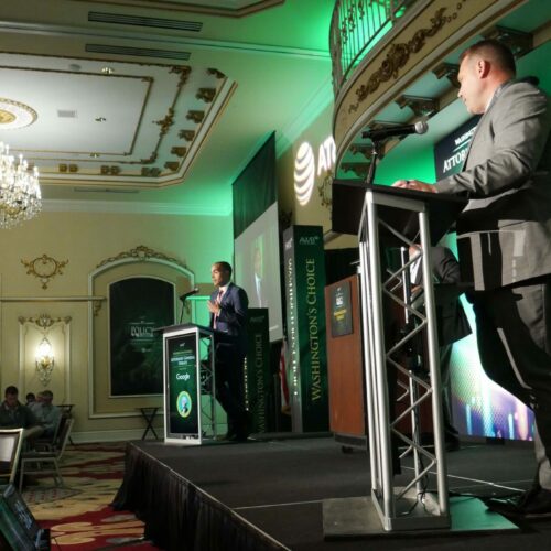 Two men, each behind a podium, stand on a stage.