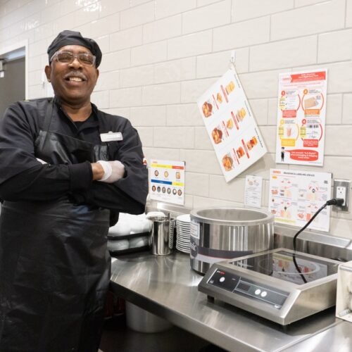 A man in a black chef's outfit stands in a kitchen.