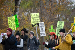 A group of people are walking, carrying brightly colored signs. Some of them read "Cougs demand cash out of carbon" and "Support WSU's fossil fuel divestment."