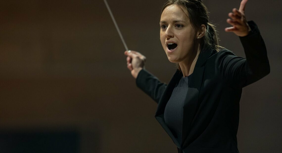 A woman holds a conductor's baton. She is conducting an orchestra.