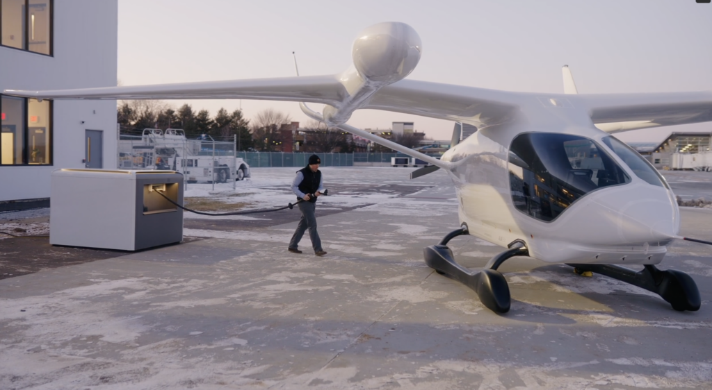 A man in a black vest and beanie walks over to an electric airplane.