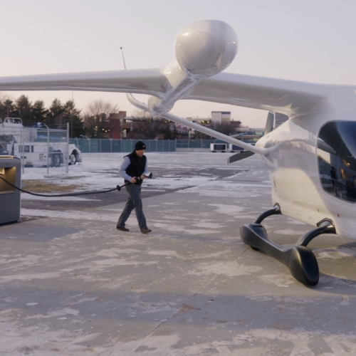 A man in a black vest and beanie walks over to an electric airplane.