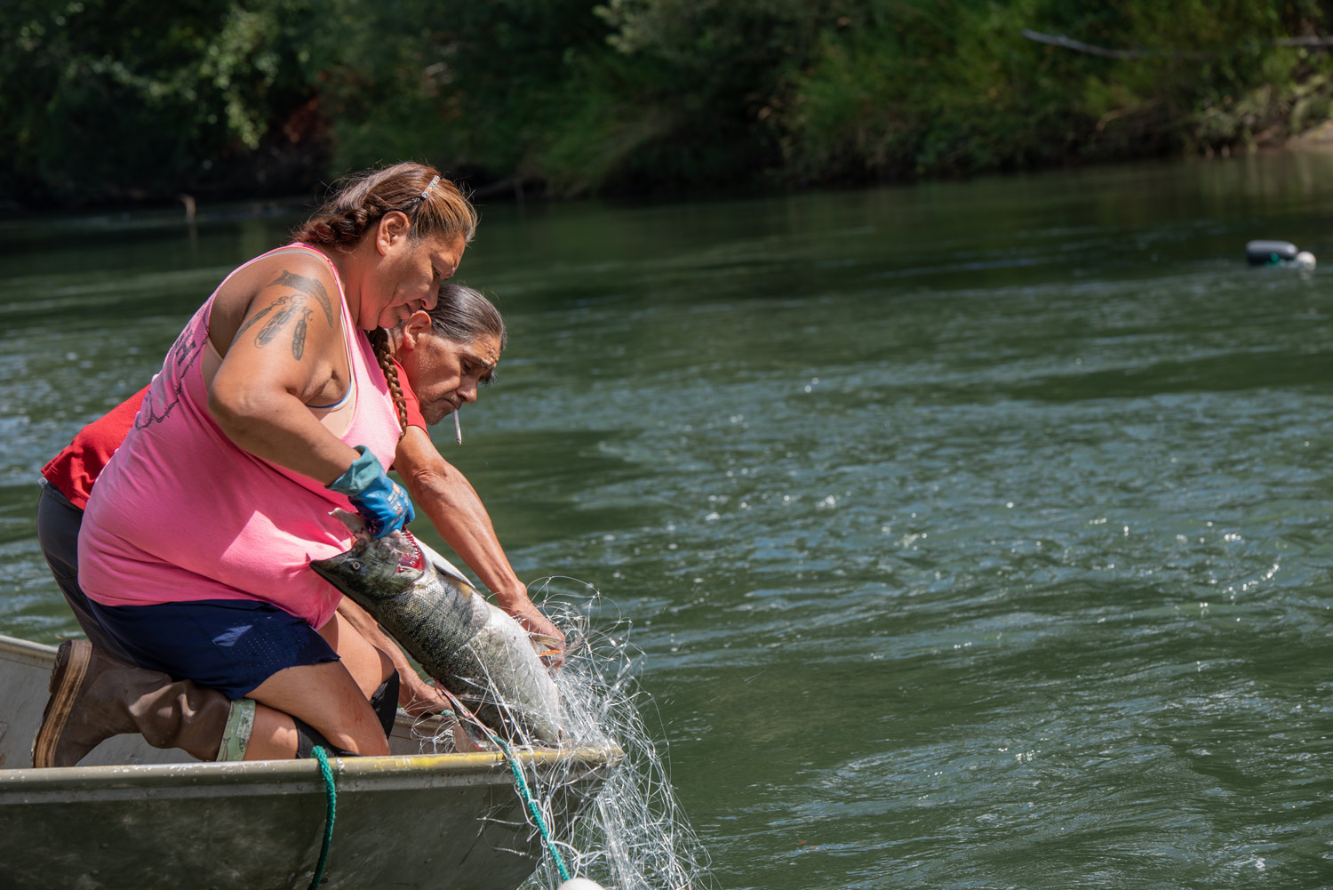 a man and woman lean over a boat to pull in a fish from a net