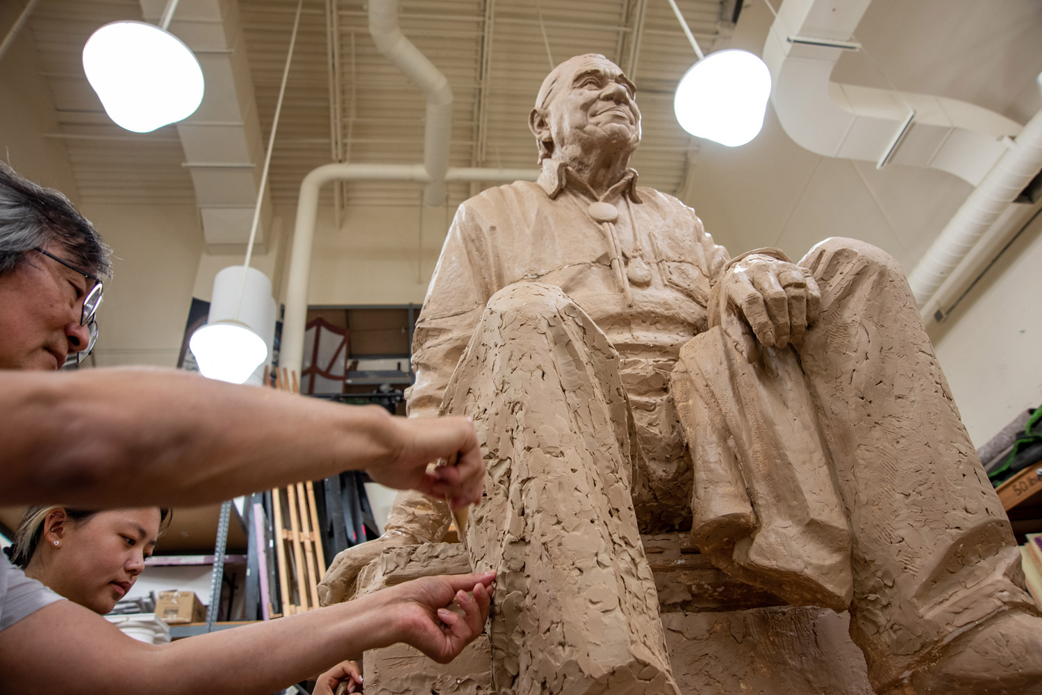 a man and girl with arms outstretched add clay to a large statue of Billy Frank Jr.