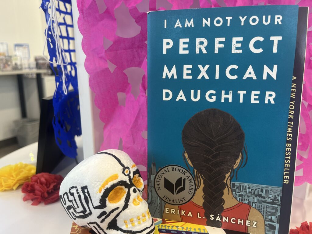 The book "I Am Not Your Perfect Mexican Daughter" is on display next to a calavera.