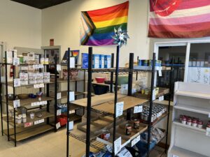 Several racks of canned goods are pictured in a room. Above the racks is a pride flag.