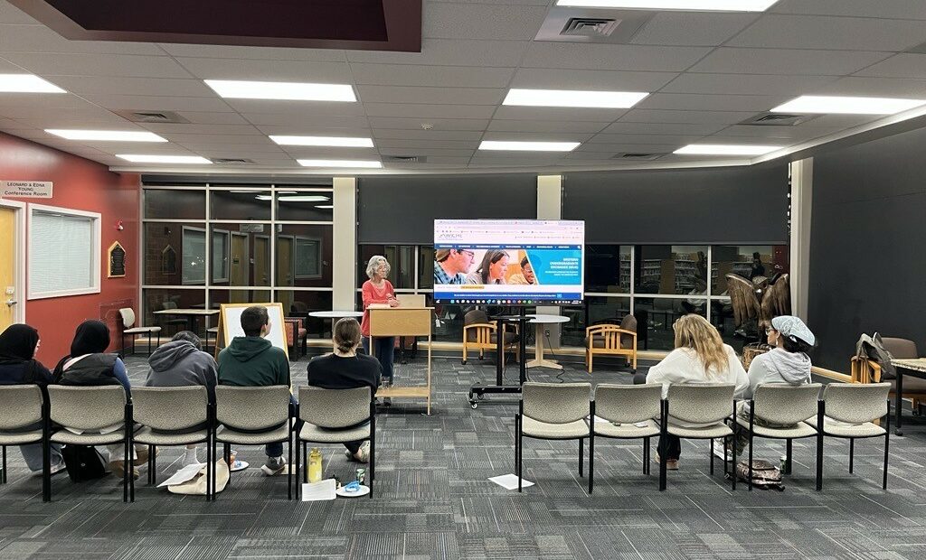 A woman presents a slideshow about college to a group of high school students at a public library.