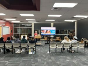 A woman presents a slideshow about college to a group of high school students at a public library.