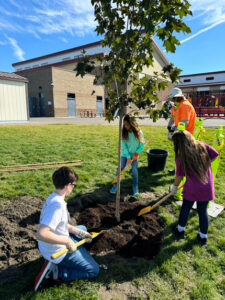 Quentin Cameron, Jaxi Mango and Taylee Kraft plant their tree, which they named Mango Rose Mac and Cheese. (Credit: Courtney Flatt / NWPB)