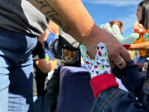 An adult hand is helping a child put on lady bug gardening gloves.