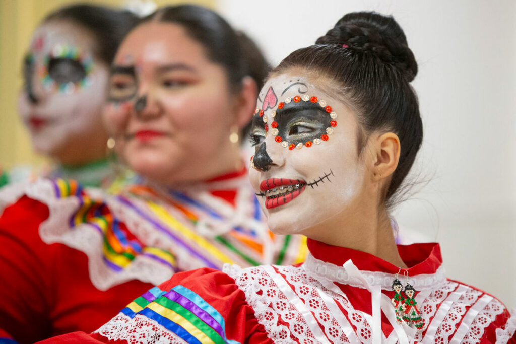 Three girls, in a folklorico dance group, pose for a photo.