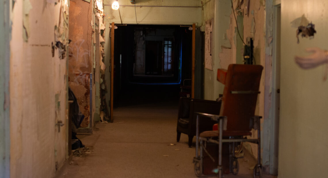 A hallway in an old hospital is pictured. The end of the hallway is dark.