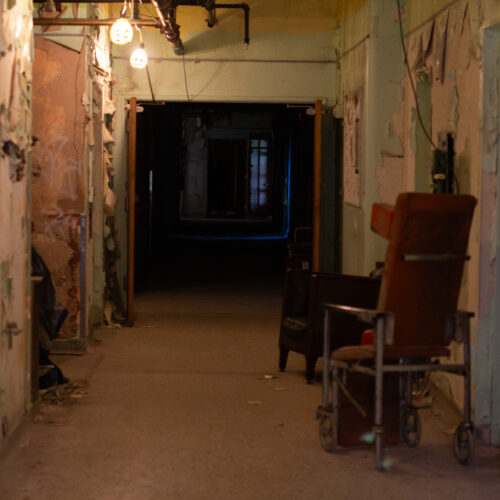 A hallway in an old hospital is pictured. The end of the hallway is dark.