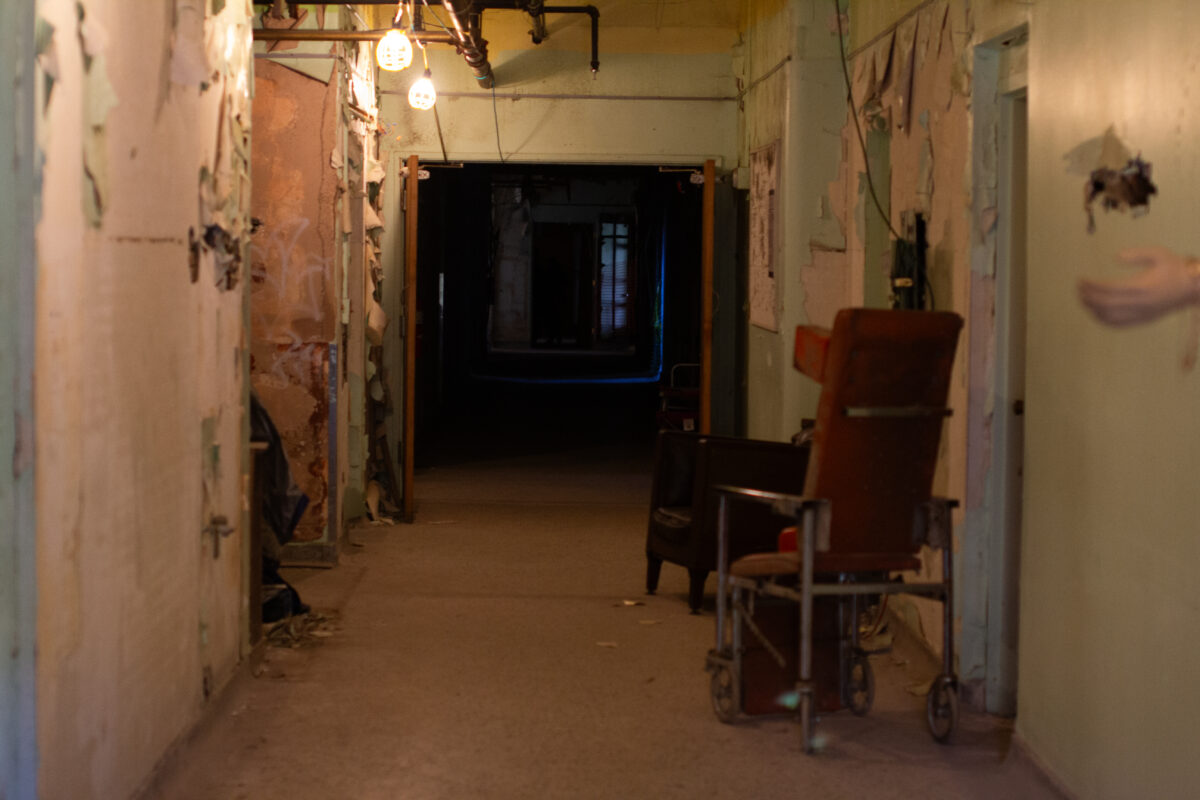 A hallway in an old hospital is pictured. The end of the hallway is dark.