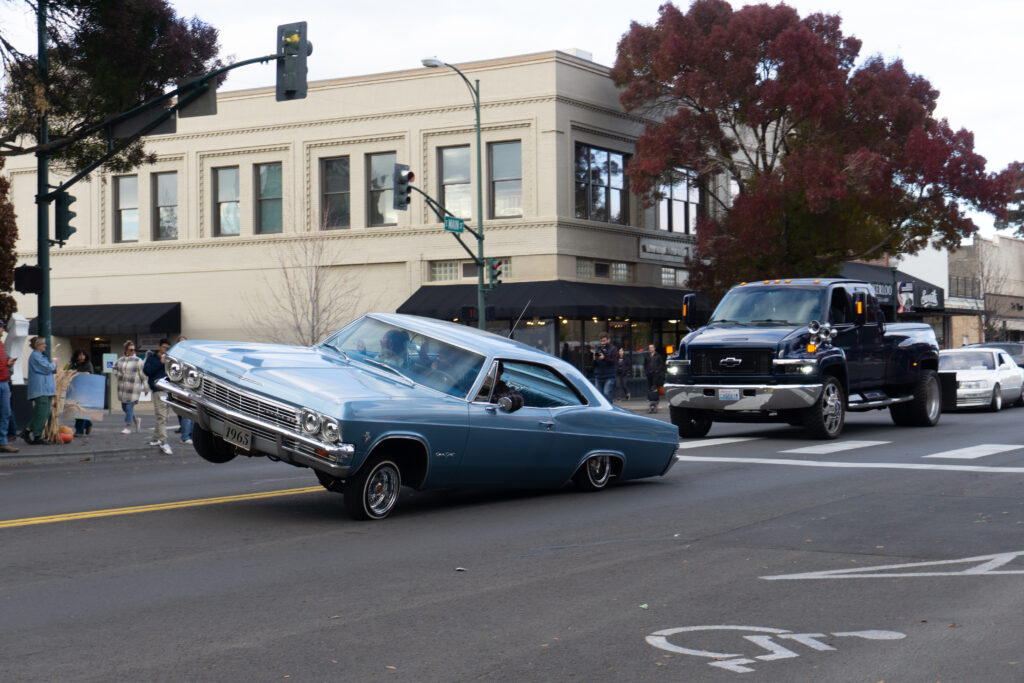 A blue car tilts on its side in a parade