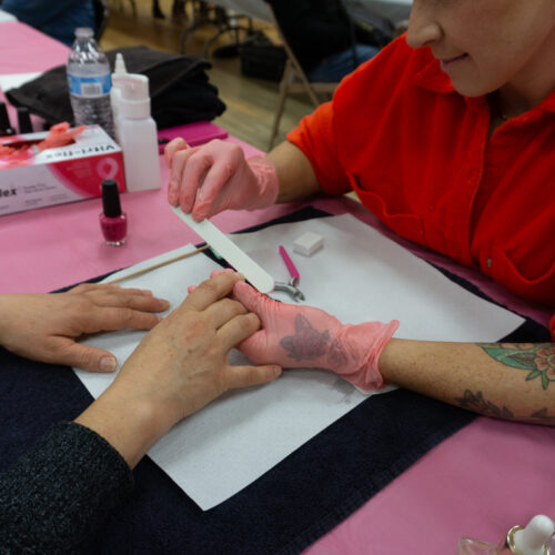 A woman in a red shirt gives a manicure.