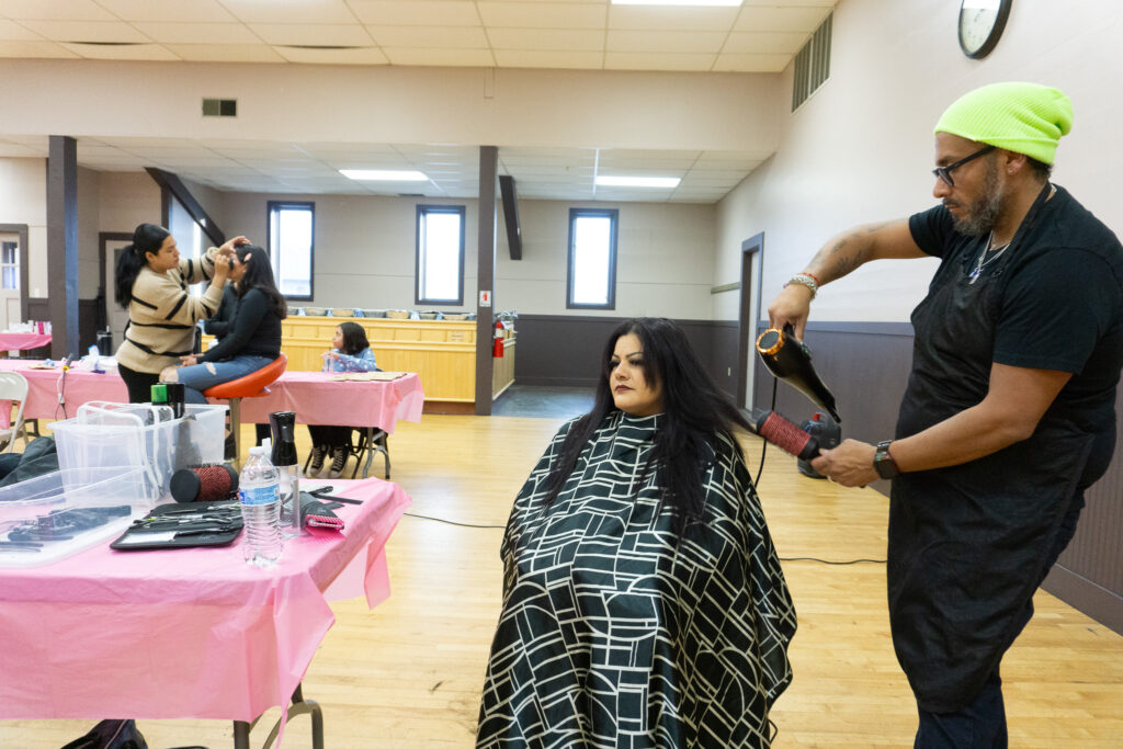 A man in a green beanie blow dries a woman's long black hair.