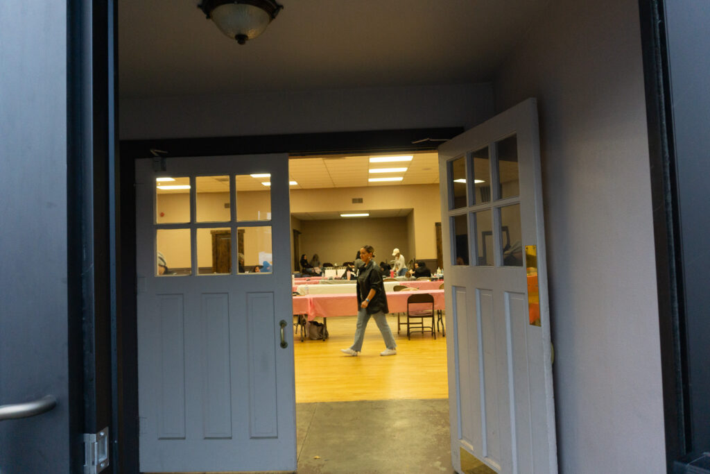 A woman in a black shirt walks past a table covered in a pink tablecloth.