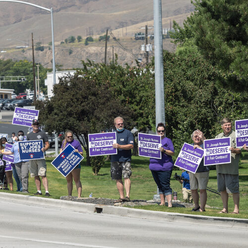 A group of people gather on the side of the road. They are holding purple signs that read "St. Joseph nurses deserve a fair contract."