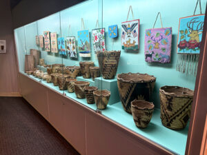 An exhibit of old woven baskets sits behind glass. There are at least 12 woven baskets of varying sizes. They all appear to be woven out of tan and brown material.