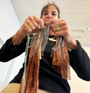 A woman in a black shirt is holding yarn in her hands. The yarn is falling down toward the camera.