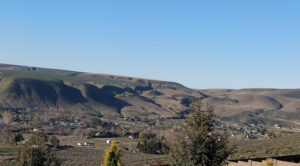 A brownish, greenish ridgeline with a few white houses dotted in front of it. The sky is blue.