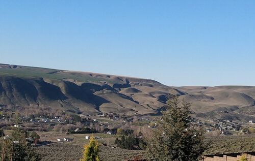 A brownish, greenish ridgeline with a few white houses dotted in front of it. The sky is blue.