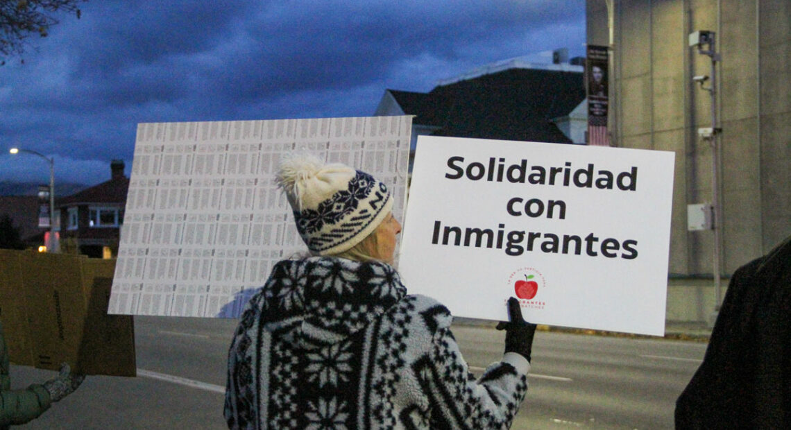 A woman wearing a knit hat holds a sign that reads "solidaridad con immigrantes."