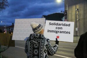 A woman wearing a knit hat holds a sign that reads "solidaridad con immigrantes."