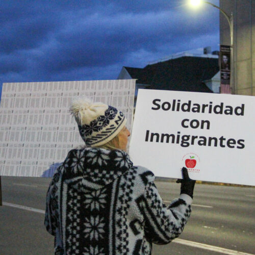 A woman wearing a knit hat holds a sign that reads "solidaridad con immigrantes."